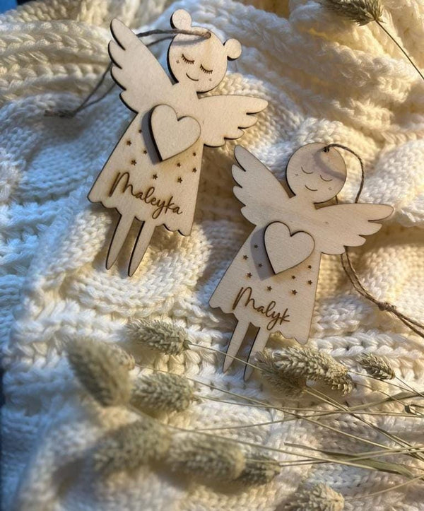 Zwei personalisierte Schutzengel aus Holz mit den gravierten Namen Maleyka und Malyk auf einer weißen Strickdecke
