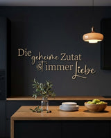 Holzschriftzug „Die geheime Zutat ist immer Liebe“ in Natur an der dunklen Wand einer modernen Küche