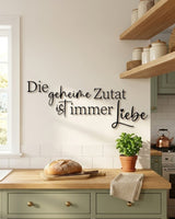 Holzschriftzug „Die geheime Zutat ist immer Liebe“ in Schwarz in einer Landhausküche mit salbeigrünen Fronten