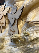 Personalisierter Schutzengel aus Holz mit Namen Malyk, aufgehängt an einer Kordel vor heller Strickdecke