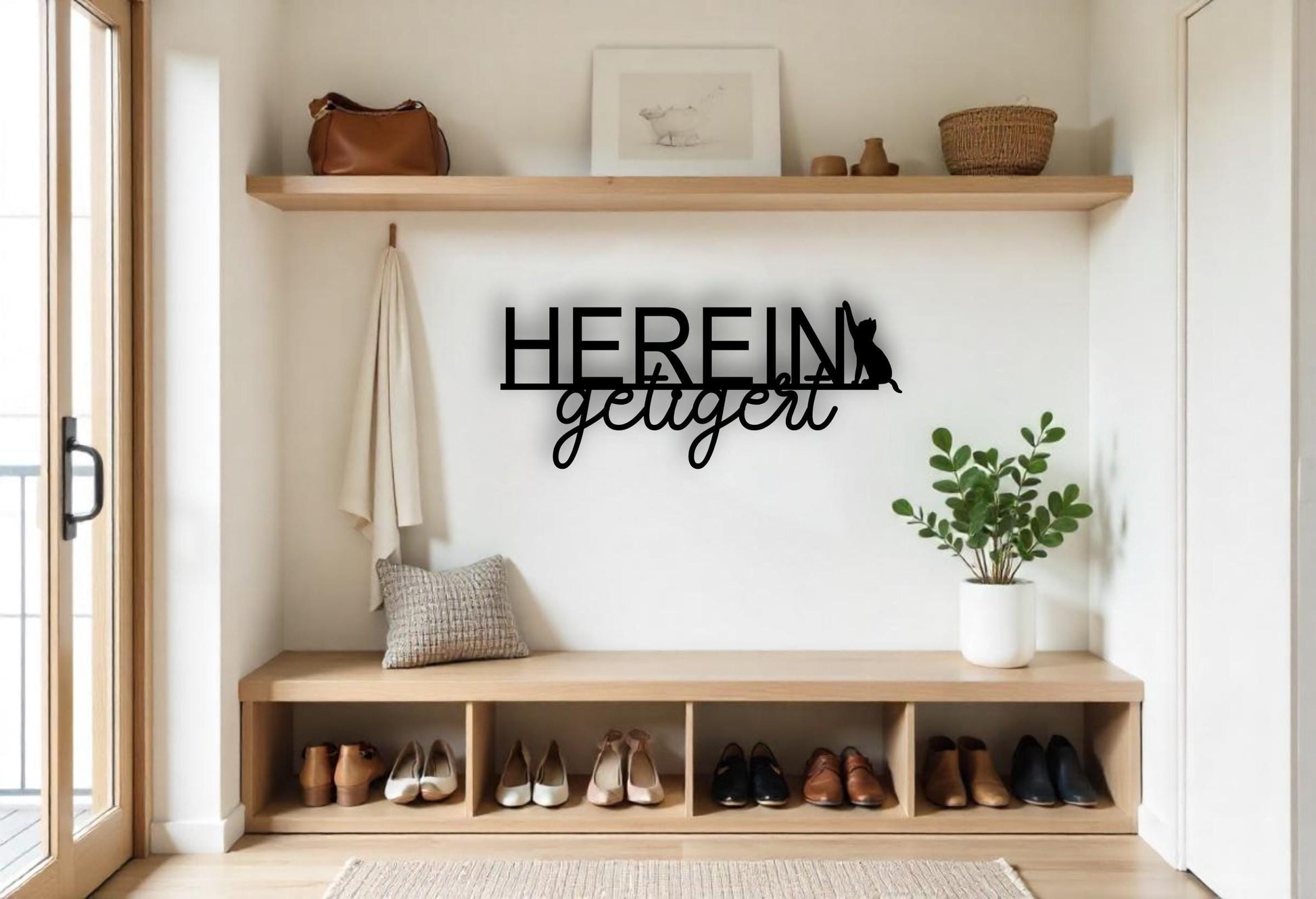 Könnte beinhalten: Schwarze Metall-Wandkunst mit den deutschen Worten "HEREIN getigert" und einer Katzen-Silhouette. Das Schild ist über einer Holzbank mit Schuhen, einem Kissen und einer Pflanze in einem weißen Topf angebracht. Eine Ledertasche und ein gerahmtes Bild befinden sich auf einem Regal.